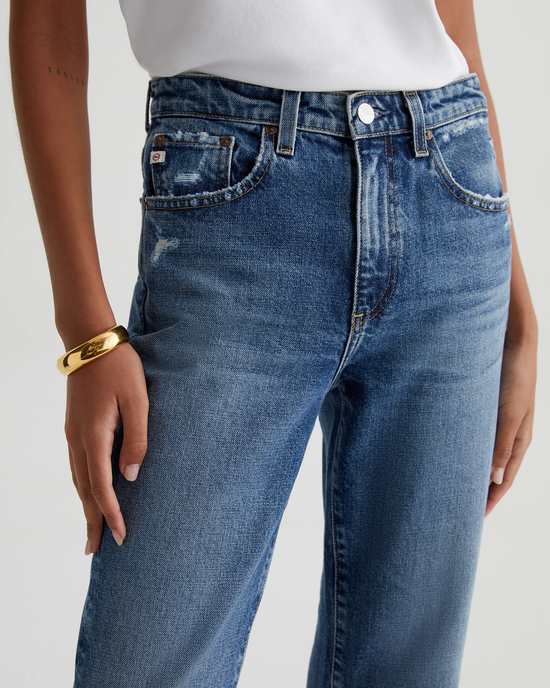 Close-up of a person wearing AG Jeans' Kinsley in 15Ys Upstate with a gold bracelet on the wrist.