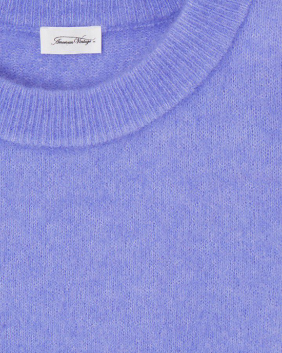 Close-up of a blue Vito Crop Sweater in Iris Chine by American Vintage with a designer crewneck label.