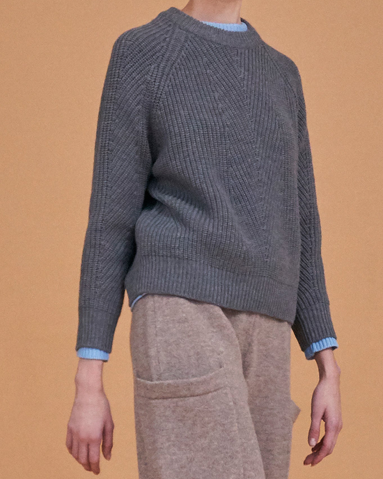 Person wearing a Chelsea Raglan Wool Sweater in Heather Grey by Demylee and beige pants against a tan background.