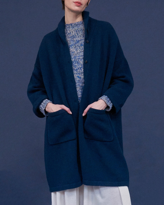 A person in a Dark Indigo Jabre Cardigan by Demylee over a patterned sweater, standing against a gray background.