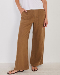 Woman wearing Not Monday's Serena Linen Pant in Espresso and a white top, standing with one hand on her hip.