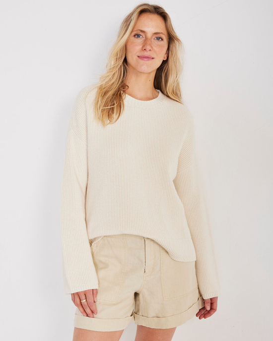 Woman wearing a Not Monday Simon Fisherman Crewneck in Ecru spring sweater and beige shorts standing against a white background.