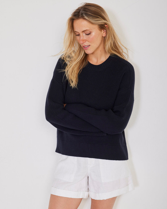 Woman in a dark Simon Fisherman Crewneck in Navy by Not Monday and white shorts standing with arms crossed.