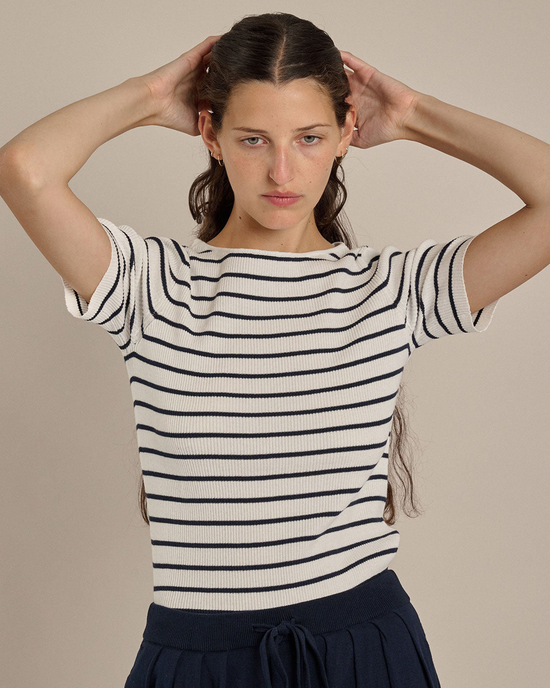 A woman in a Demylee Rena Stripe Top in Off White/Navy adjusting her hair with both hands.