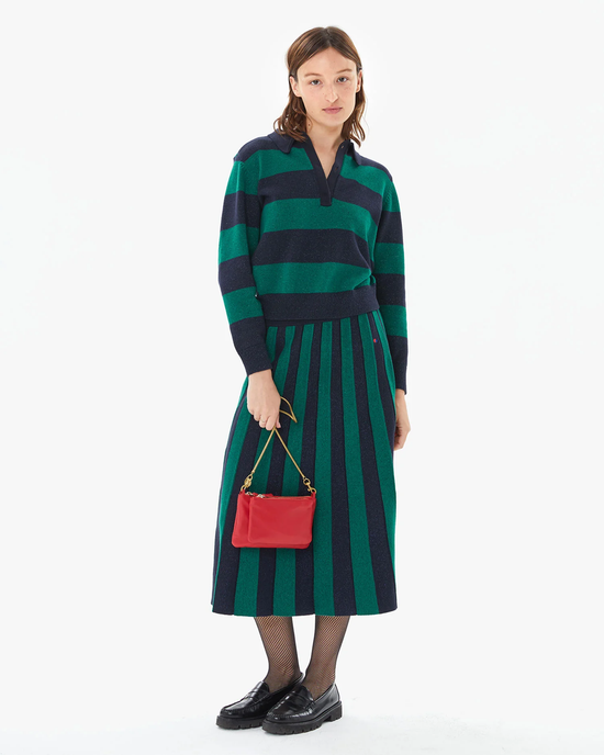 Woman posing in a green and navy striped sweater and skirt set with a Clare V Wallet Clutch Plus in Rouge Nappa handbag and black shoes.