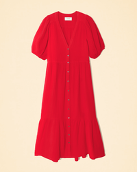 Red short-sleeved Lennox dress in Real Red with buttons and a ruffled hem on a beige background, made from Cotton Gauze by XiRENA.