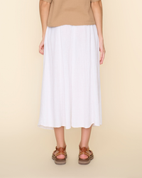 A person standing wearing a white cotton gauze XiRENA Deon Skirt in White and brown sandals against a beige background.