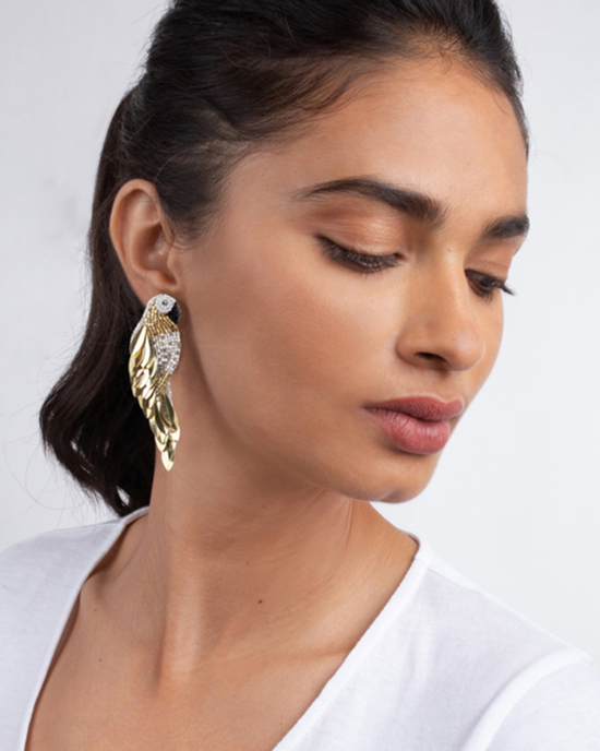 A woman wearing a white top and a large Olivia Dar Ara Earrings in Gold adorned with micro seed beads & sequins.