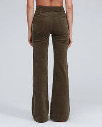 A person stands with their back to the camera, wearing ASKK NY Brighton Corduroy Wide Leg pants in Safari Green with back pockets, set against a plain light gray background.