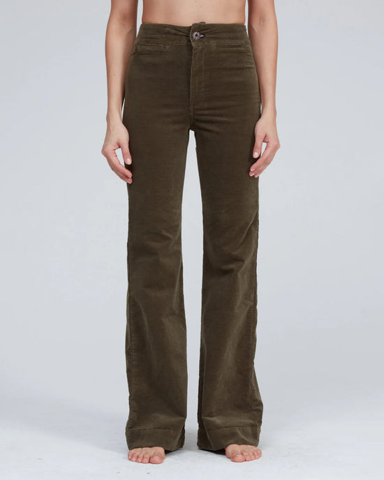 A person stands barefoot in ASKK NY Brighton Corduroy Wide Leg pants in Safari Green, featuring a wide leg and flared silhouette, against a plain light background. Only the lower body is visible; the upper body and head are not shown.