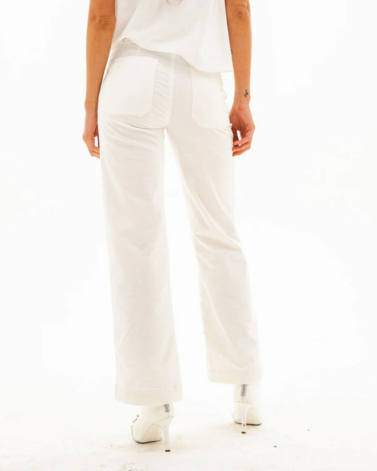 A person stands facing away, wearing ASKK NY Sailor Corduroy in Eggshell—white high-rise pants with two back pockets, one with ruching—paired with a white top and heels against a plain white background.