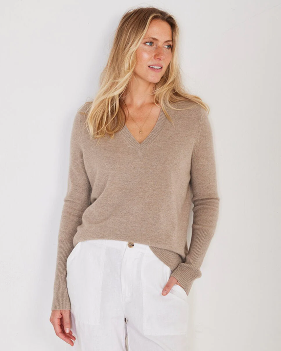 Woman in a Not Monday Ava Cashmere V Neck in Latte sweater and white pants posing against a white background.