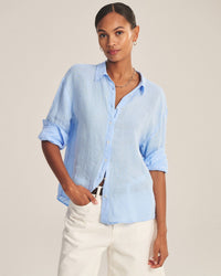 A woman wears the Velvet by Graham & Spencer Brighton Long Sleeve Button Up in Sailboat with white pants, standing against a plain background and gazing confidently at the camera.