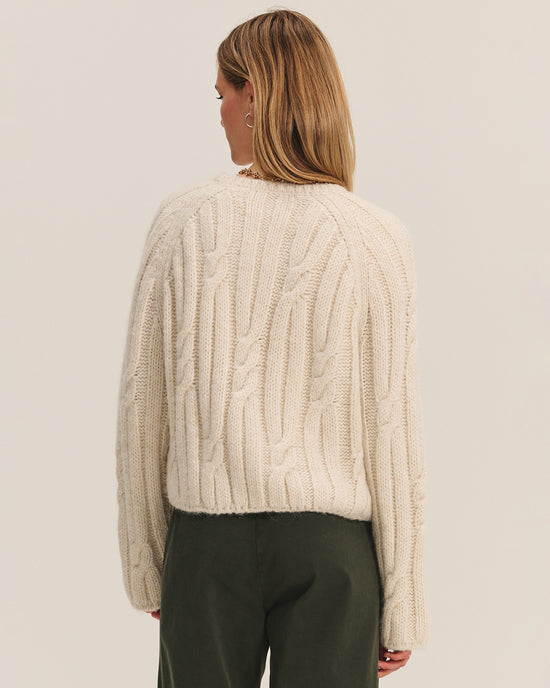 A person with shoulder-length light brown hair is shown from the back, wearing the Marina Long Sleeve Crew Top in Ivory by Velvet by Graham & Spencer and olive green pants against a plain light background.