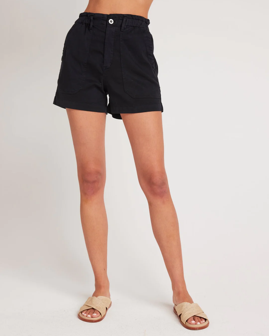 Callie Ruffle Short in Vintage Black by Bella Dahl with an elastic ruffled waistband and beige sandals on a person against a neutral background.