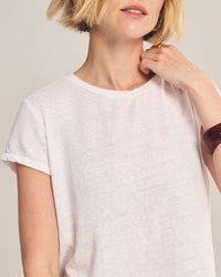 A person with short blonde hair wears the Velvet by Graham & Spencer Casey Short Sleeve Crew Neck Top in White, touching their neck with one hand. Only their upper body appears against a neutral background.