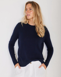 A woman in a Chase Cashmere Crewneck in Navy from Not Monday and white pants looking to the side.