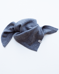 The COLORI Small Triangle Bandana in Kensington, a soft gray 100% cashmere knit with a small white tag, is loosely folded on a white surface with its ends spread outward.