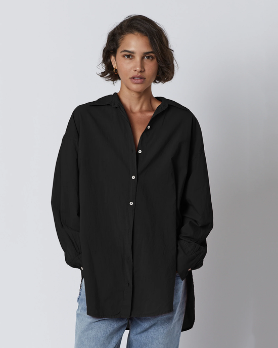 Woman in a Velvet by Graham & Spencer Redondo L/S Button Up in Black oversized shirt, and blue jeans standing against a white background.