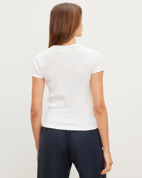 Woman standing with her back to the camera, wearing a white Brenny S/S Rib Top in White by Velvet by Graham & Spencer and dark trousers.