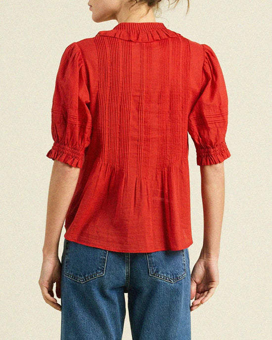 A person is seen from the back in a Trovata Birds of Paradis Jess Blouse in Crimson Check, featuring puffed ruffle half sleeves, paired with blue jeans, set against a light background.