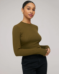 A woman in a Bella Dahl Long Sleeve Crop Crew Neck in Deep Rosemary and black pants standing against a neutral background.
