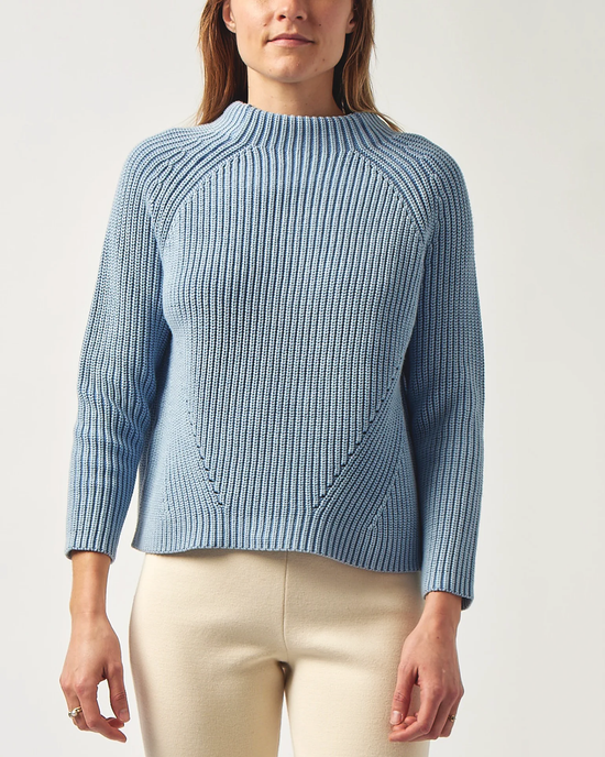 Woman wearing a blue Demylee Daphne Cotton Sweater in Sky Blue with an asymmetrical pattern and light-colored pants.