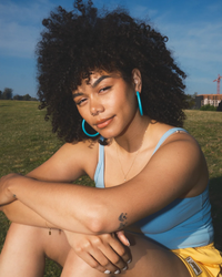 Young woman with curly hair enjoying the outdoors, wearing B&L hand-carved mango wood C Hoop in Large earrings and a casual outfit.