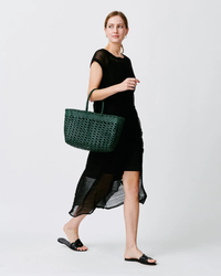 A woman in a black dress holding a green Dragon Diffusion Cannage Kanpur Big handwoven leather tote bag in Forest Green.