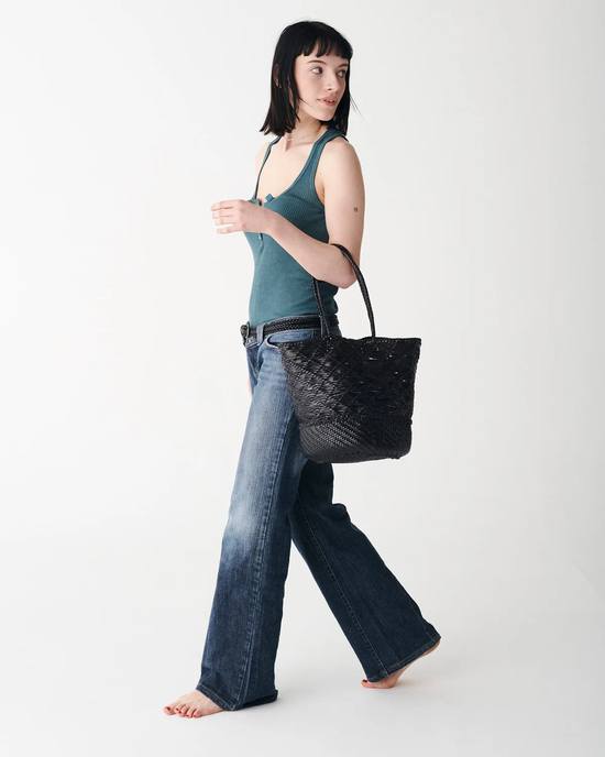 Woman walking in a studio, wearing blue jeans and a tank top, carrying a black Dragon Diffusion Corso Bucket Bag.