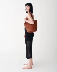 Woman posing in a black dress with side cut-outs, carrying a large woven Dragon Diffusion Corso Bucket Bag in Tan.
