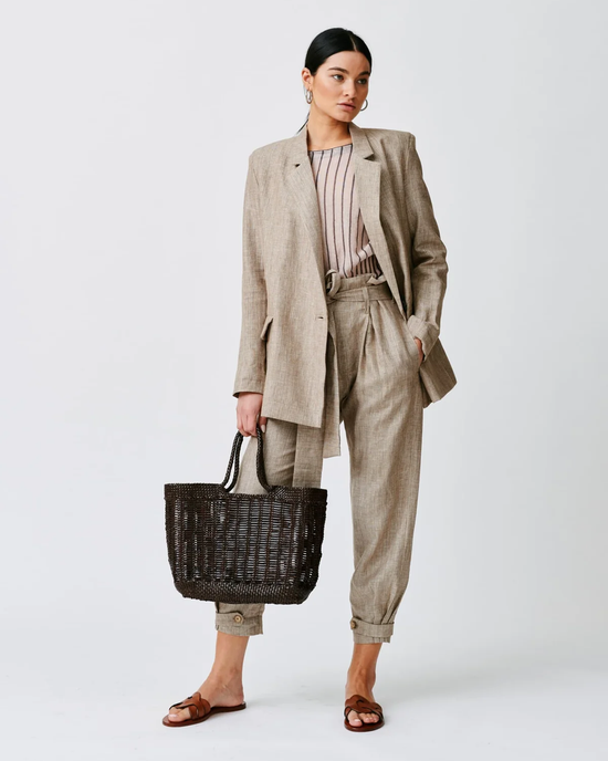 A woman modeling a beige business-casual suit with a striped shirt, carrying a large Dragon Diffusion Window Basket in Dark Brown bag made of 100% leather, and wearing sandals.