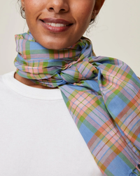 A person wearing a white top and a colorful Mois Mont Scarf No 722 in Nordic Blue tied around the neck.