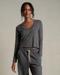 A woman wears the perfectwhitetee Fiona L/S Recycled V Neck Charcoal top with matching grey recycled cotton drawstring sweatpants, standing against a neutral background.