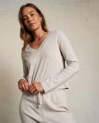 A woman wearing the perfectwhitetee Fiona Long Sleeve Recycled V Neck in Silver and matching drawstring pants stands against an off-white wall, looking confidently at the camera.