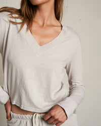 A woman stands against a plain background wearing the perfectwhitetee Fiona Long Sleeve Recycled V Neck in Silver. Her head is slightly tilted and her face partially out of frame.