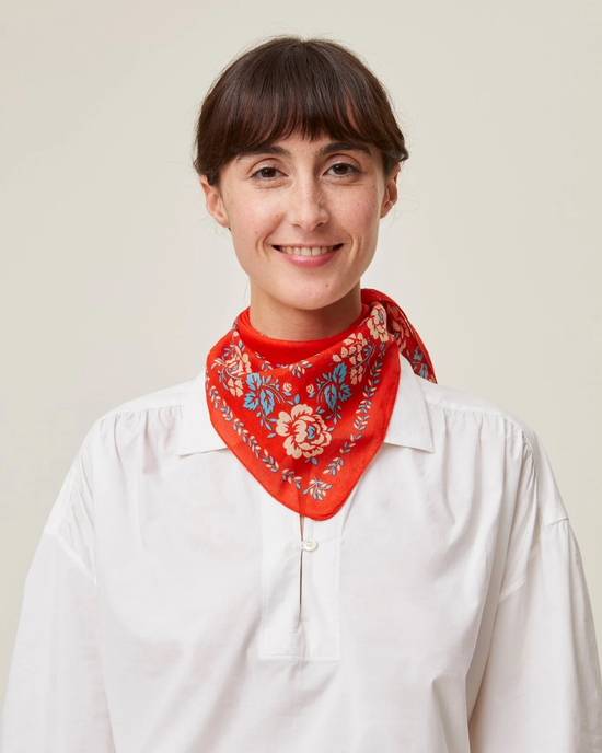 Woman in white shirt with Red Cotton Floral Bandana No 652 in Poppy Red by Mois Mont, smiling at the camera.