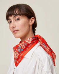 A woman with a side-parted haircut wearing a white shirt and a red Mois Mont cotton floral Bandana No 652 in Poppy Red handcrafted in India, tied around her neck.