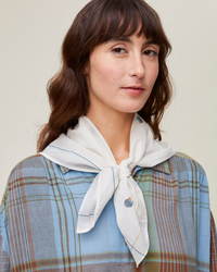 Woman with a handcrafted Mois Mont Bandana No 656 in Natural tied around her neck over a plaid shirt.