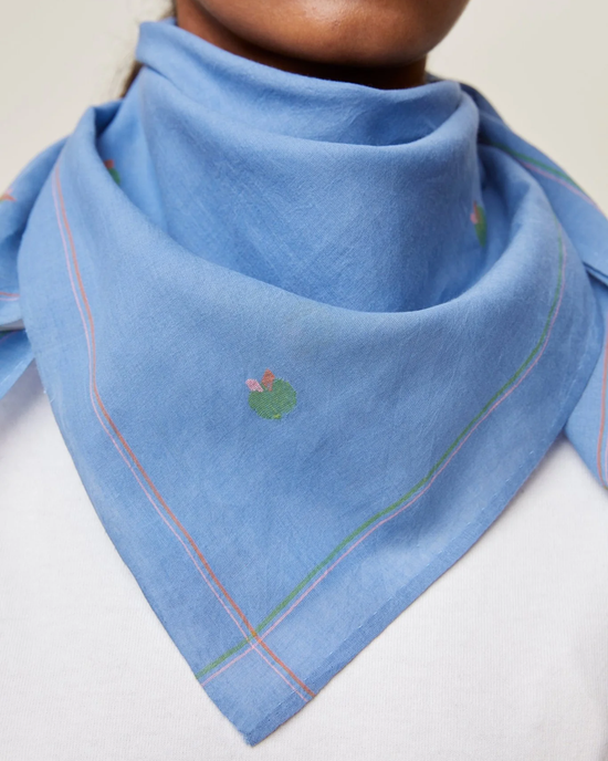 A person wearing a light blue Bandana No 656 in Nordic Blue scarf with a subtle floral pattern and colorful stitched borders by Mois Mont.
