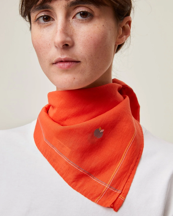 A woman wearing a handcrafted in India, orange Jamdani Bandana No 656 in Poppy Red with a small emblem by Mois Mont.