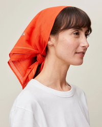 A woman in a white shirt wearing a Mois Mont Bandana No 656 in Poppy Red over her head, looking to the side.