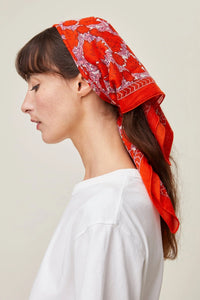 Woman with a Mois Mont Bandana No 680 in Poppy Red and white top, side profile view.