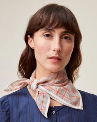 A woman with a fringe wearing a blue striped shirt and a Mois Mont Bandana No 712 in Poppy Red neck scarf.
