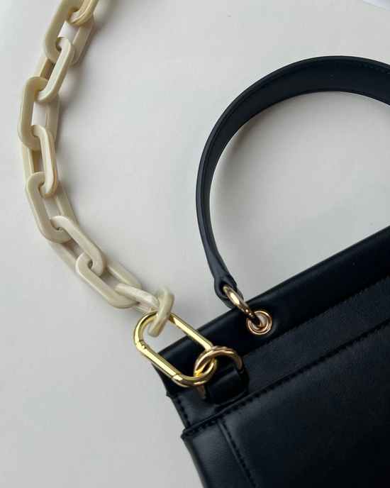 Close-up of a black handbag with a gold-colored ring connecting a Machete Alabaster handbag chain.