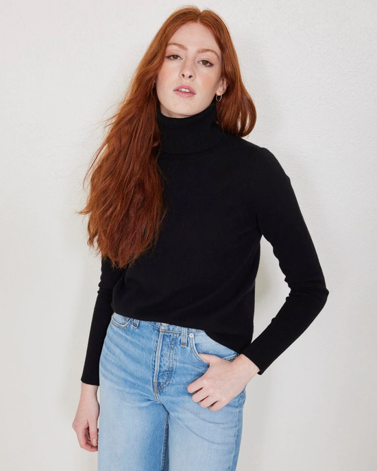 A woman with long red hair wearing a black Not Monday Hayden Turtleneck in a classic fit and blue jeans.