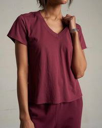 A person models the perfectwhitetee Hendrix Cotton S/S Boxy V Neck Tee in Dark Burgundy with matching pants, standing against a plain background and highlighting the tee’s crisp cotton texture.