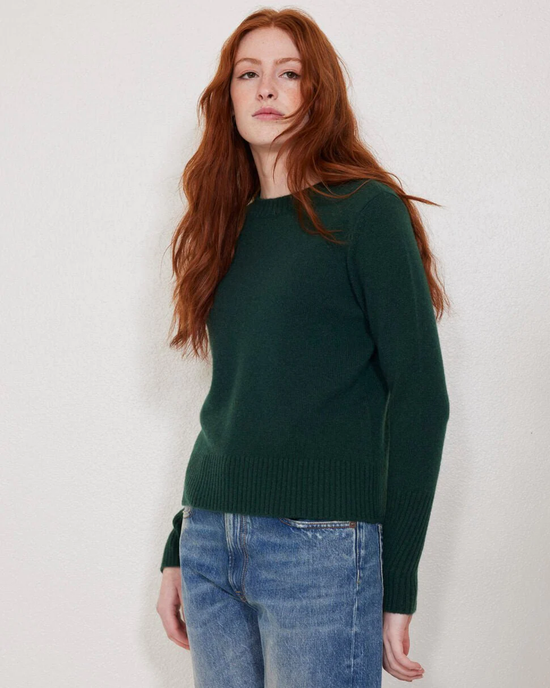 Woman in a Not Monday Jane Crewneck in Jade cashmere crewneck sweater and blue jeans standing against a plain background.
