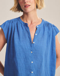 A woman with short blonde hair wears the Janey Ruffle Short Sleeve Button Down in Bluejay by Velvet by Graham & Spencer, styled with a delicate necklace and shown from the shoulders up against a plain background.