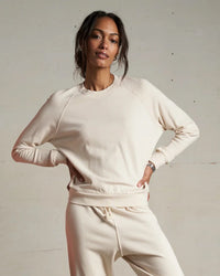 A woman in the Alexi French Terry Sweatshirt in Sugar by perfectwhitetee stands confidently with one hand on her hip and the other at her waist, posing against a plain background.